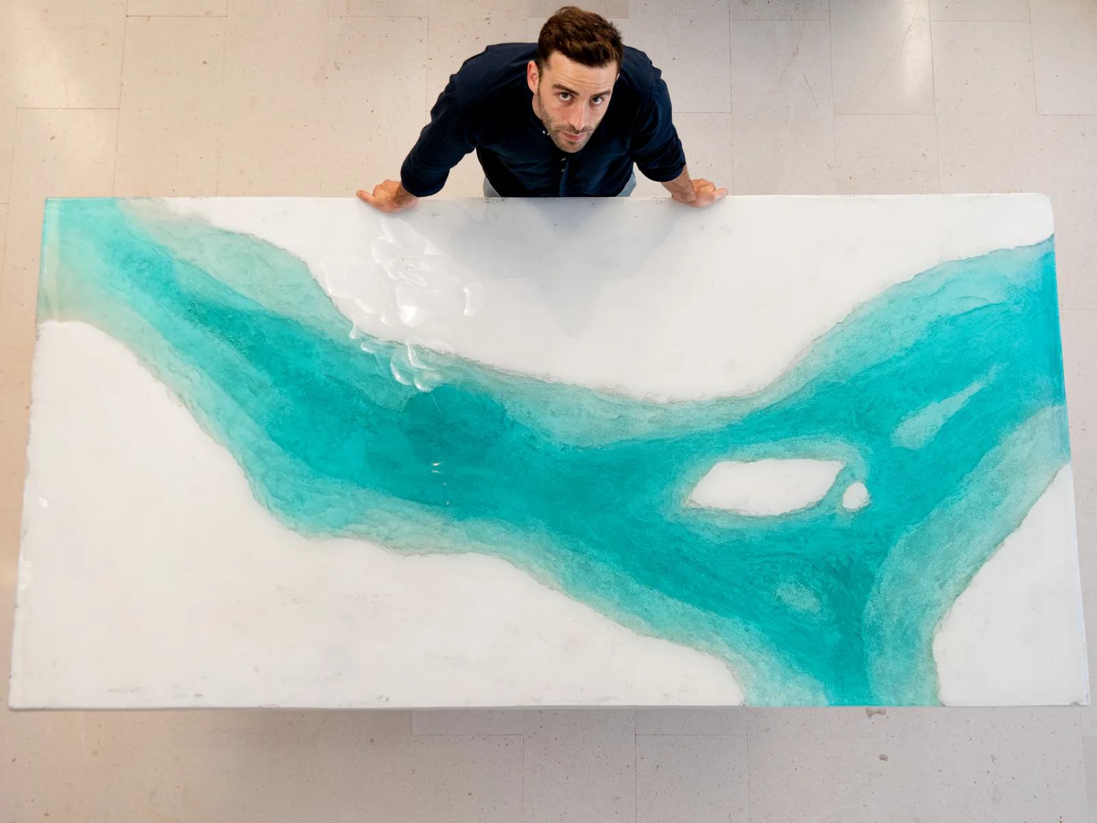 Álvaro Varela, visto desde arriba, apoyado en una gran obra blanca y turquesa en forma de río.